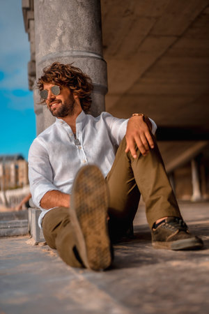 Summer lifestyle with a young dark-haired Caucasian man with long beard, sunglasses and a white...