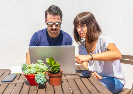 A couple confined at home making a video call with some friends with the computer, on the terrace of...