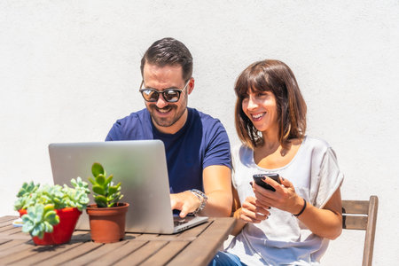 A couple confined at home making a video call with some friends with the computer, on the terrace of...