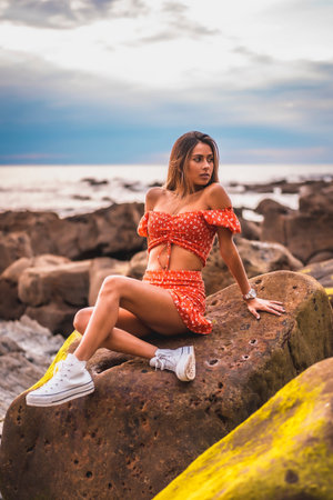 A young brunette Caucasian woman in a red dress on the beach of Itzurrun in the town of Zumaia,...