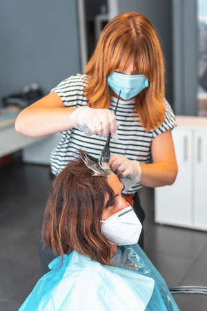 Hairdresser with mask dyeing gray hair to the client. Safety measures for hairdressers in the Covid-19 pandemic. New normal, coronavirus, social distanceの写真素材
