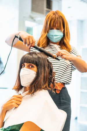 Hairdresser with mask and client, looking at camera. Reopening with security measures for hairdressers in the Covid-19 pandemic. New normal, coronavirus, social distanceの写真素材