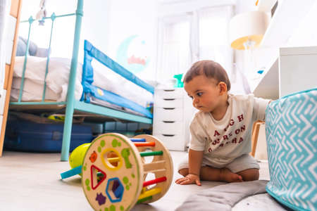 Young Caucasian mother playing with her in the room with toys. Baby less than a year learning the first lessons of her mother. Boy playing on the floor with toysの写真素材
