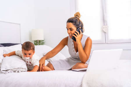 Young Caucasian mother with her son in the room on top of the bed. Mother teleworking and caring for her child, a new normal after the coronavirus pandemic, covid-19. Social distanceの写真素材