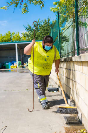 Worker in a recycling factory or clean point and garbage with a face mask and with security protections, new normal, coronavirus pandemic, covid-19. Sweeping the inside of the enclosureの写真素材