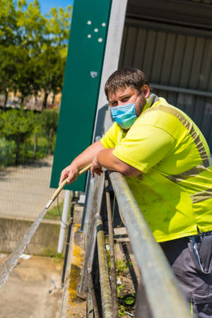 Worker in a recycling factory or clean point and garbage with a face mask and with security protections, new normal, coronavirus pandemic, covid-19. Portrait of worker cleaning with hoseの写真素材