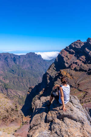 A young woman sits resting and looking at the views of the Roque de los Muchachos national park on top of the Caldera de Taburiente, La Palma, Canary Islands. Spainの写真素材