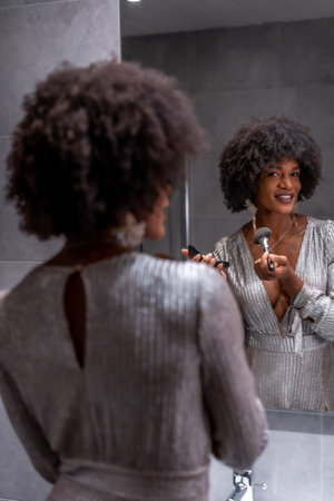 A young black girl with afro hair putting on makeup before the party with a smile. Exclusive party,...