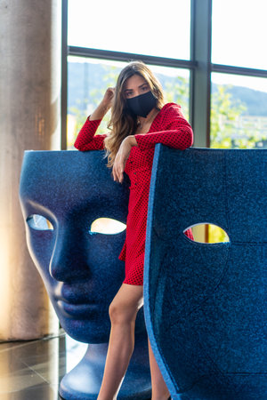 Young blond Caucasian woman with a face mask and a red dress doing sightseeing in the city. New normality, social distance, covid-19 pandemic, coronavurisの写真素材