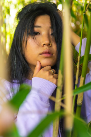 a young Asian girl inside some beautiful bamboo in a park with a pink sweater