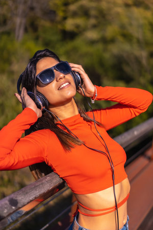 Lifestyle, brunette Caucasian girl enjoying music with headphones in a park. Young girl in red...