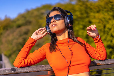 Lifestyle, brunette Caucasian girl enjoying music with headphones in a park. Young girl in red...