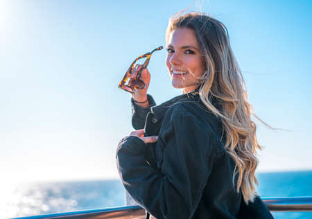 Lifestyle, a blonde on the beach at sunset with the sun in the background. Summer posing in a gray dress and black jacketの写真素材