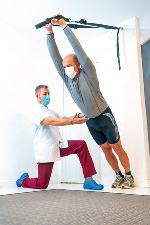 Patient assisted by a Physiotherapist with a face mask performing stretching. Physiotherapy with...