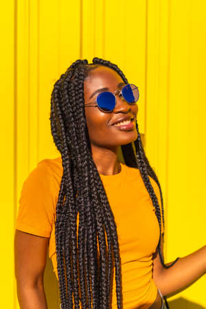 Lifestyle, attractive black girl with long braids, yellow t-shirts and short jeans on a yellow background. With sunglasses having fun, trap dancerの写真素材