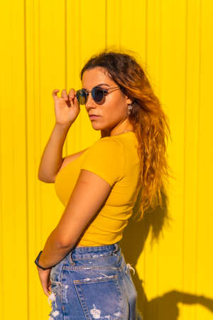 Lifestyle, Caucasian blonde girl in yellow t-shirts and short jeans on a yellow background. Fashionable pose of the attractive with seductive gaze, street photographyの写真素材