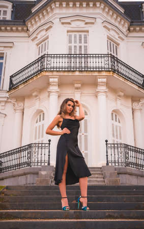 Lifestyle, blonde Caucasian in a glamorous dress and blue heels in a rustic house. The young pretty girl on the stairs of the white houseの写真素材