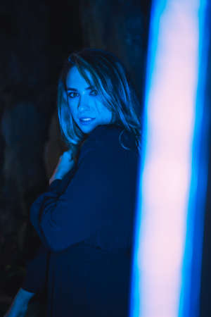 Lifestyle, a young Caucasian blonde in a black dress in a photo inside a cave, illuminated with blue led light. With soft diffuse light on the sideの写真素材