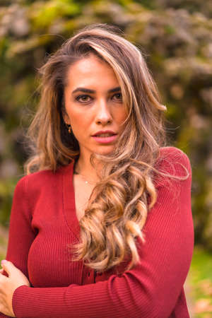 Autumn lifestyle, blonde Caucasian girl in red sweater and gorgeous black American hat, enjoying nature in park with big trees, portrait of young model smilingの写真素材