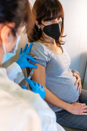 A young pregnant woman receiving the coronavirus vaccine. Antibodies, immunize population. side effects, risk people, antibodies, new normal, covid-19. Vertical photoの写真素材