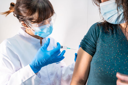 A woman doctor with a face mask applying the coronavirus vaccine, the patient with fear of the...