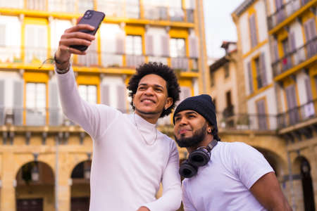 Lifestyle, two black Latino friends taking a nice selfie on the street. Boy with afro hair and boy with hat and earphonesの写真素材
