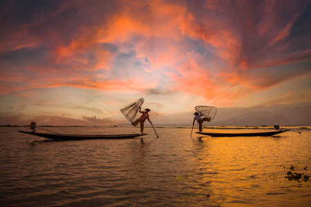 Inle Lake, Myanmar '; spring of 2018: two traditional fishermen of Lake Inle Lake, one white and the other orange raising the net crouched in front of the photographerのeditorial素材