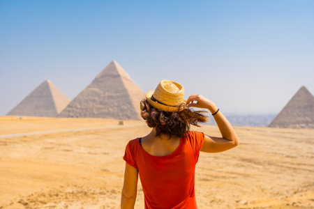 A young tourist in a red dress looking at the Pyramids of Giza, the oldest Funerary monument in the world. In the city of Cairo, Egyptの写真素材