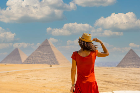 A young tourist in a red dress looking at the Pyramids of Giza, the oldest Funerary monument in the...