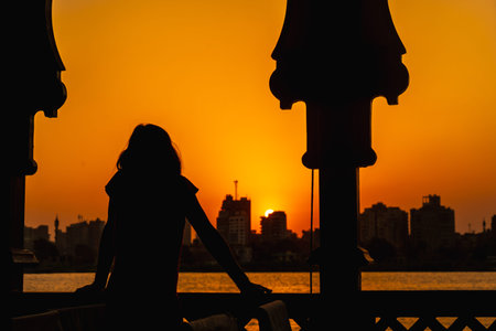 A young woman looking at the orange sunset on the Nile River from a boat leaning on the railing, the...