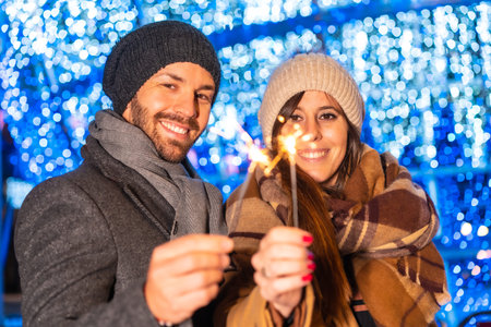 Winter portrait of a Caucasian couple enjoying the Christmas lights with torches in hand, lifestyle