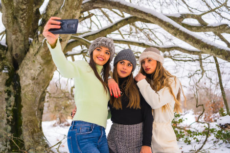 Winter lifestyle, three beautiful caucasian friends taking a selfie with the phone in the snow under...