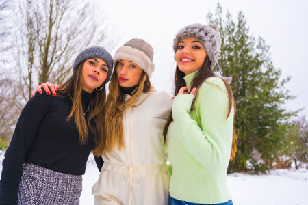 Winter lifestyle, young caucasian friends with winter outfit and wool hats enjoying the snow next to snowy pine trees, holidays in natureの写真素材