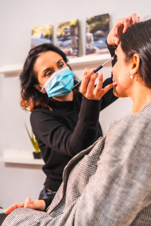 A makeup artist with a face mask with the concealer brush. Security measures of aesthetic centers in...