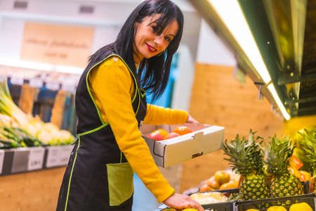 Portrait of brunette fruit girl working ordering fruits in a greengrocer establishmentの写真素材