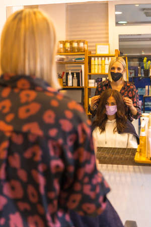Hairdresser with face protection mask showing the result of the hairstyle to the client. Security measures in the Covid-19 pandemic, vertical photoの写真素材