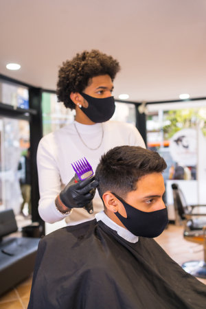 Hairdresser with afro hair with mask and gloves cutting client's hair with razor. Security measures of Hairdressers in the Covid-19 pandemicの写真素材