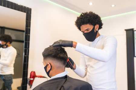 Young hairdresser with mask and gloves cutting hair. Security measures of Hairdressers in the Covid-19 pandemicの写真素材