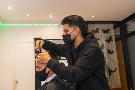 Hairdresser with face mask cutting hair of young client. Security measures of Hairdressers in the Covid-19 pandemicの写真素材