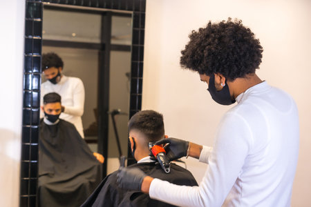Hairdresser with mask and gloves cutting the hair of the young client. Security measures of Hairdressers in the Covid-19 pandemicの写真素材