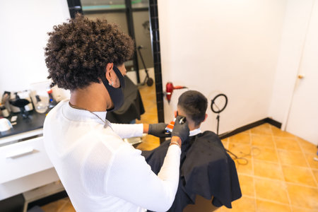 Young hairdresser with mask and gloves cutting client's hair with razor. Security measures of Hairdressers in the Covid-19 pandemicの写真素材