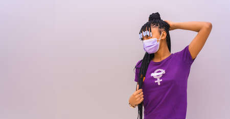 International women's day in the year of the  pandemic . Dominican woman with feminist purple shirt and face mask, gray plain background with copy and paste spaceの写真素材