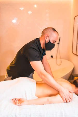 Massage at home, performing a massage at the client's home on the forearms. With a face mask in the pandemicの写真素材
