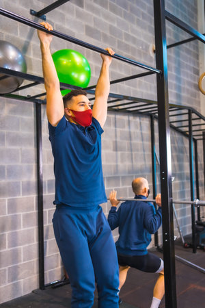 Two young people doing strength exercises in the gym in the  pandemic, a new normal. With protective...
