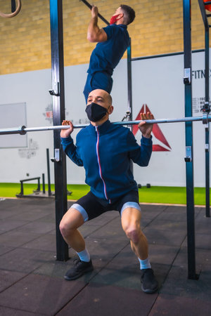 Two young people doing strength exercises in the gym in the  pandemic, a new normal. With protective face maskの写真素材