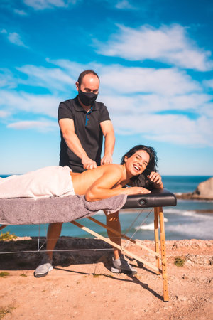 Massages on the coast near the sea, masseuse with face mask in the pandemic