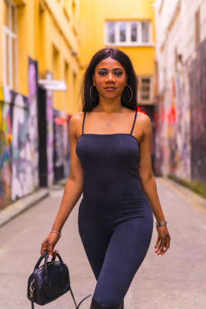 Fashionable urban style with a black African girl in a black suit and high boots on a city street. Strolling with a black bagの写真素材