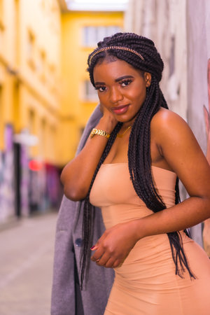 Trendy urban style with a black African girl in a cream colored dress on a city street. Portrait of the young pretty girl with braidsの写真素材