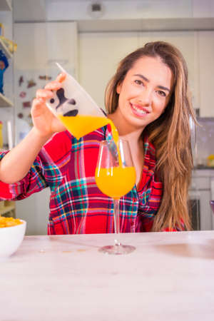 Healthy lifestyle, pretty blond Caucasian woman in a red plaid shirt helping herself to a fresh orange juice for breakfastの写真素材