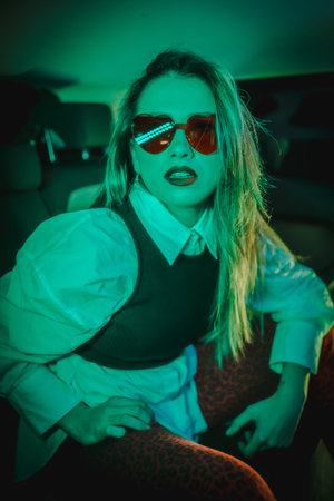 Urban photography with green neons in the back of a car of a young blonde Caucasian model with heart...